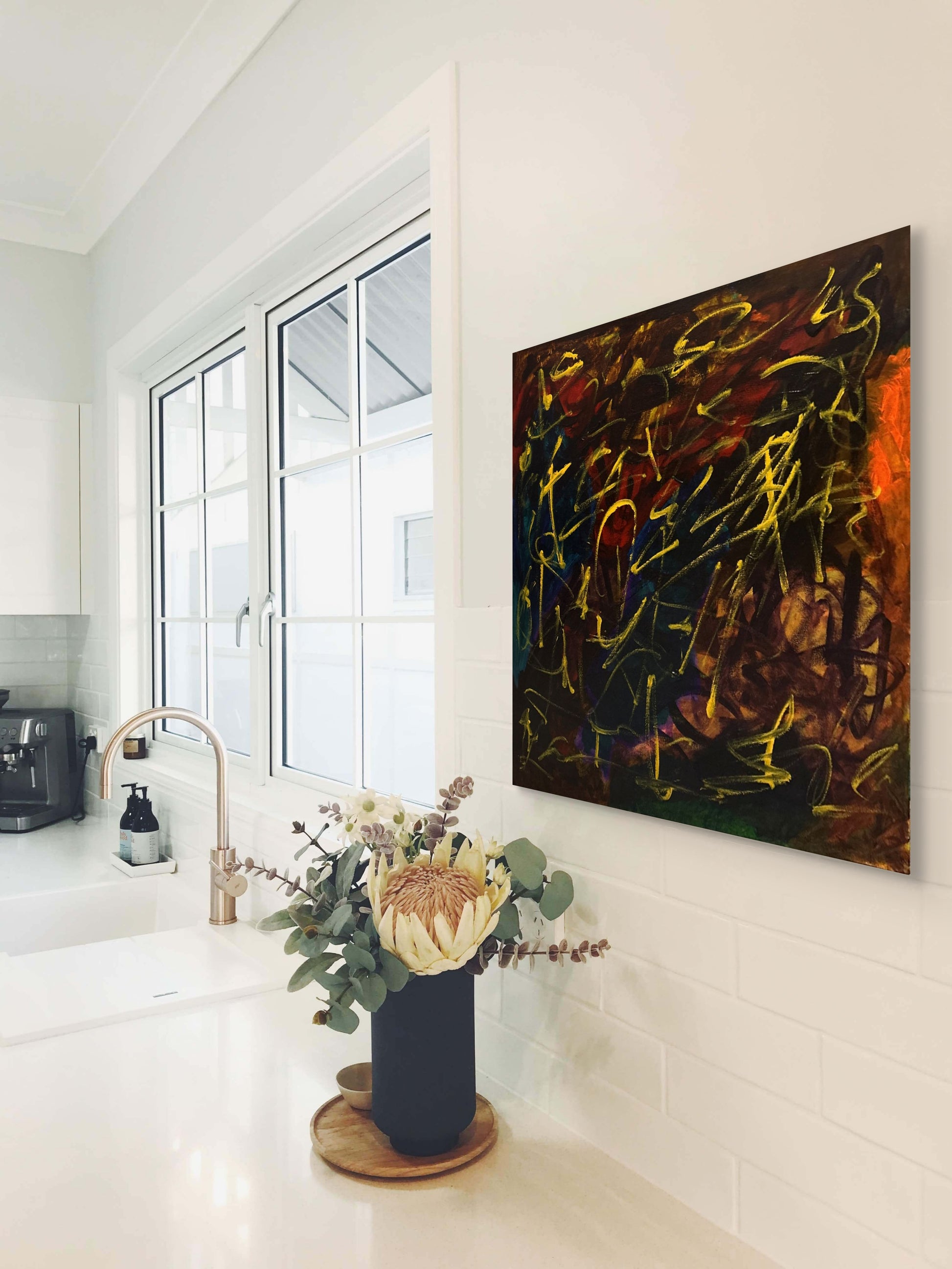 Modern kitchen with abstract painting on the wall and a vase with flowers on the counter.