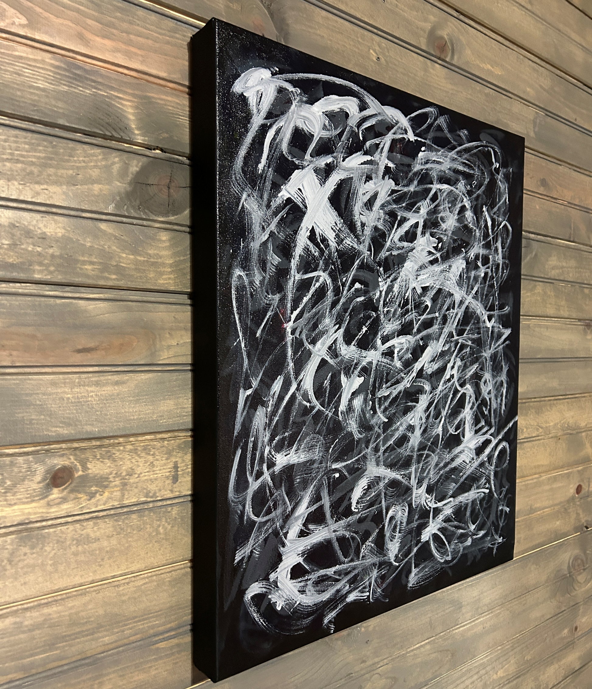 Abstract white painting on a black canvas against a wooden wall