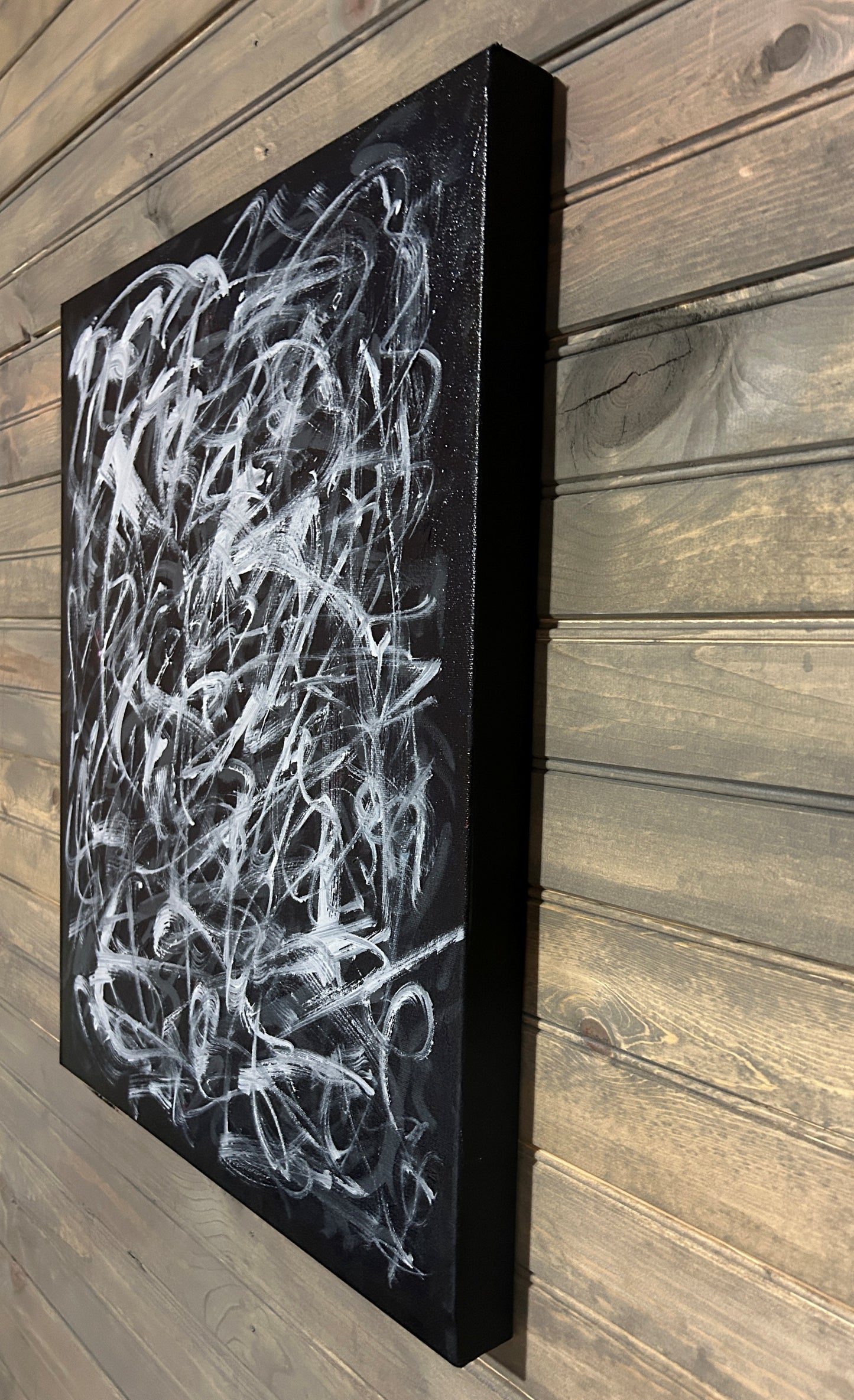 Abstract white painting on a black canvas against a wooden wall