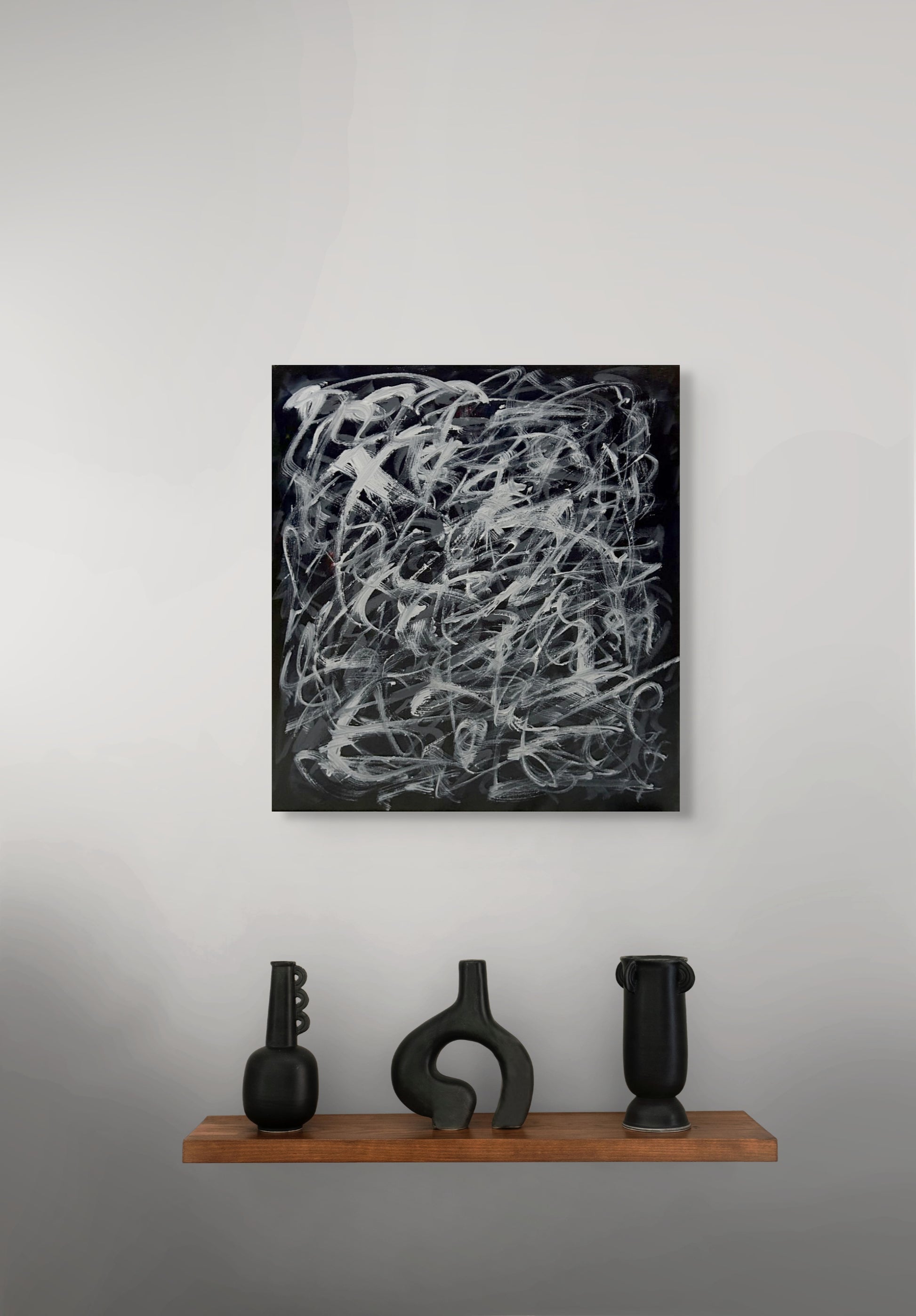 Abstract black and white painting on a gray wall with three black vases on a wooden shelf below.
